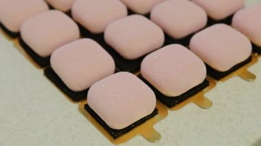 Şekerci, modern kremalı kekin üstüne pembe renkli kadife kremayla yenebilir altın renkli folyo süsü ekliyor. Zarif kare kadife pasta, içinde fındık ve meyve var. Kapat.