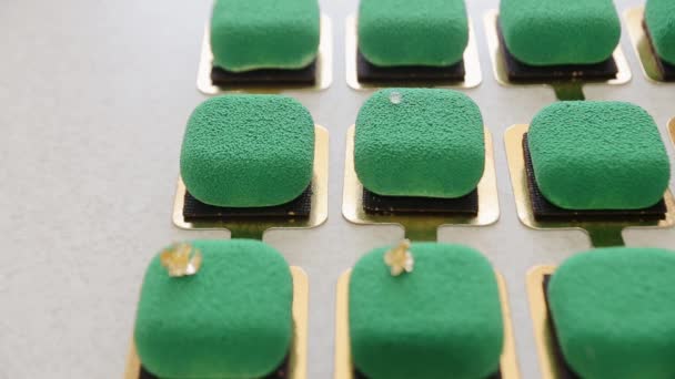 Suikerbakker voegt een eetbaar goudkleurig folie decor element toe aan de bovenkant van moderne mousse cake met velours glazuur. Elegantie vierkante velours mousse cake, noten en fruit vulling binnen — Stockvideo