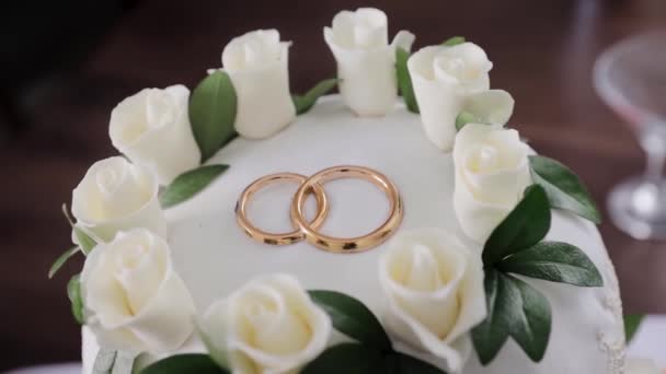 Un hermoso pastel de bodas decorado con anillos de oro.Pan de pastel blanco para la boda. El concepto de postres festivos — Vídeo de stock