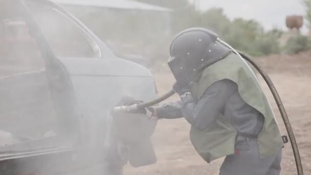 一个穿着防护服头戴硬礼帽的男人用一缕沙子加工金属 穿着喷砂制服的工人 — 图库视频影像