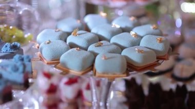 Cam tepside turkuaz kekler ve kurabiyeler. Dikey çekim. Kurabiye üzerinde mavi krema olan çikolatalı kekler.