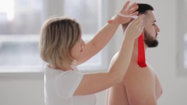 Bir omuz sakatlığından sonra sporcunun engellenmesi gerekir. Doktor bir adamın omzuna kinetik bandaj yapıştırıyor..