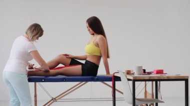 Kadın doktor, bacağına Kinesio bandı yapıştırarak kadına yardım ediyor. Bacağında kineziyoloji elastik tedavi bandı olan beyaz bir kız.