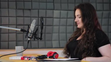 Kadın ses sanatçısı kulaklığını takıyor ve canlı yayında seyircilere merhaba diyor. Ses kayıt stüdyosunda podcast prodüksiyon süreci