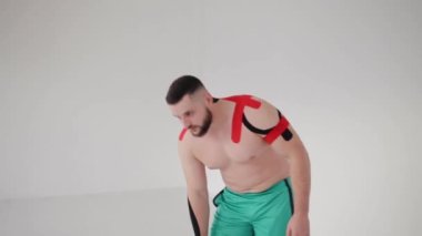 Erkek sporcu, yaralanmış vücudundaki kineziyoloji tedavisinden sonra alışılmadık hissediyor. Vücudundaki elastik tedavi bantlarını kontrol ediyor.