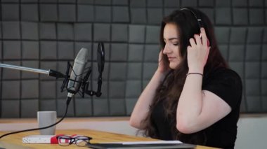 Kadın ses sanatçısı kulaklık takar, senaryoya bakar ve canlı yayına başlar. Ses kayıt stüdyosunda podcast prodüksiyon süreci