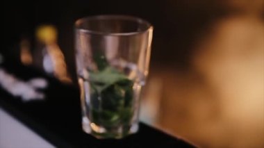 Bir barmen alkollü kokteyl mojito hazırlarken profesyonel kristal buz küplerini bardağa koyuyor. Kapat.