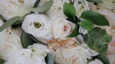 Nikah yüzüklerinin ve nişan yüzüğünün yakın plan fotoğrafı çiçek buketinin üzerinde duruyor.