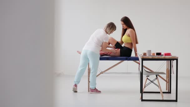 Vrouwelijke Fysiotherapeut Die Kinesio Tape Het Been Van Een Patiënt — Stockvideo