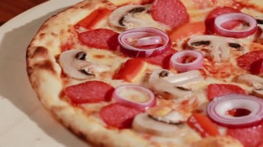 Eritilmiş peynirli, soğanlı, mantarlı, salamlı ve kırmızı biberli iyi pişmiş pizza. Tahta tabakta Capricciosa denilen tipik İtalyan pizzası.