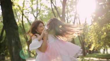 Bir anne ve kızı, güneşli bir parkta, doğa dolu bir ortamda sevgi, bağlantı ve neşe temalarını resmeden mutlu bir anı paylaşıyor.