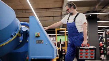 İnşaat makinelerini teftiş eden, alet çantası taşıyan, araç gereç ve malzeme arayan iş elbiseli bir adam.