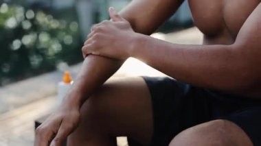 Koyu tenli bir adam koluna güneş kremi sürüyor. Açık yaz havasının tadını çıkarırken deriyi uv radyasyonundan koruyor.