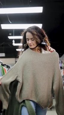 Bir kadın sıcak bir süveteri iki varyasyondan seçer. Kışlık kıyafet mağazası. Bir kadın sıcak giysileri ilgiyle seçer. Bayan alışverişkolik. Kışlık kıyafet mağazası. Dikey video