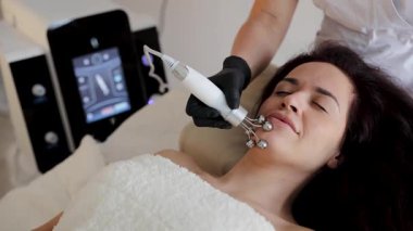 Modern bir kozmetoloji kliniğinde mikroakım cihazıyla yüz gerdirme seansı yapan bir kadın. Cilt bakımı ve yaşlanmayı önleme uzmanlığı