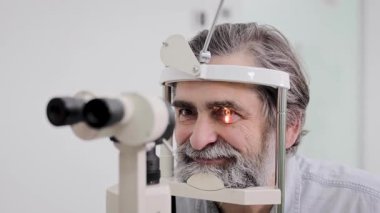 Üst düzey bir adam göz muayenesi için bir optometriste gidiyor. Detaylı görme sağlığı muayenesi için yarık lamba mikroskobu kullanıyor.