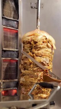 Hızlı hizmet veren bir lokantada lezzetli bir yemek hazırlamak için dönen bir tükürükten et kesen kişi. Kebap ya da shawarma dürümü için taze tavuk eti hazırlıyorum.