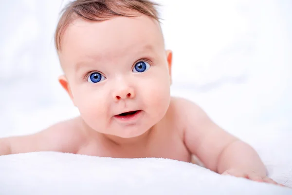 Маленький милый малыш смотрит в камеру на белой стене с голубыми глазами . — стоковое фото