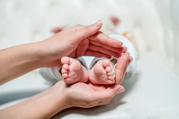 Mãe segurando os pés do bebê em um fundo branco — Fotografia de Stock