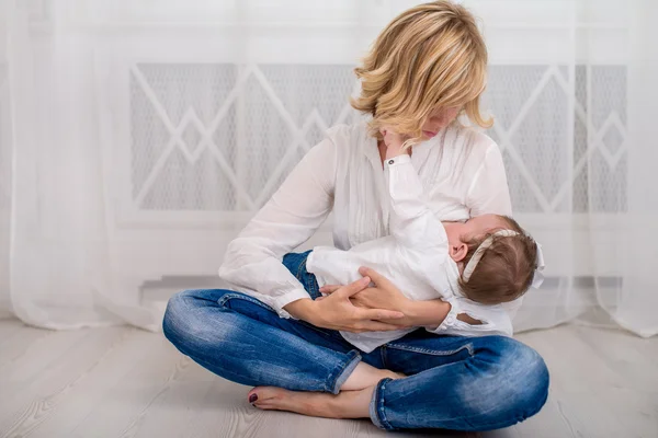 Giovane madre che allatta il suo bambino bambina sdraiata sul seno e che si nutre su uno sfondo piagnucoloso — Foto Stock