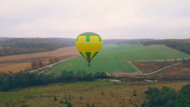 Vue aérienne par drone du vol en ballon par temps nuageux. Un ballon volant bas au-dessus du sol. Vol en montgolfière d'automne au-dessus d'une fabuleuse zone de lacs et de forêts. — Video
