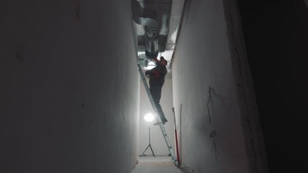 Silhouet van een bouwvakker die ventilatiekanalen aanlegt. Werknemer aan een ladder in een nieuw gebouw op een bouwplaats. — Stockvideo