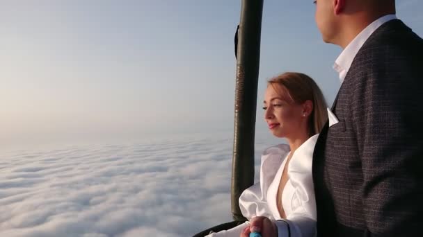 Las novias vuelan en un globo sobre las nubes. La novia y el novio toman un palo selfie en un globo sobre un fondo de la salida del sol sobre las nubes. Boda sobre las nubes. — Vídeos de Stock