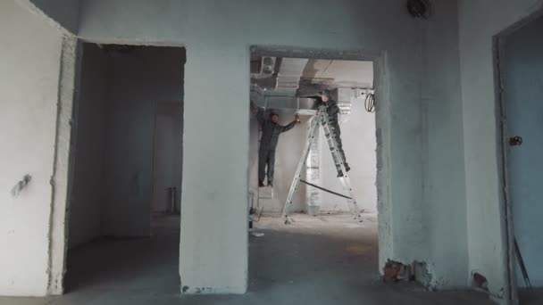 Ein Mitarbeiter, der die Installation von Lüftungsanlagen in einem neuen Haus durchführt. Der Meister steht auf einer Leiter und führt die Montage der an der Decke befestigten Gasrohre und Netze aus. — Stockvideo