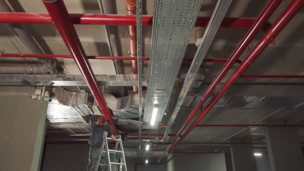 Yeni bir eve havalandırma sistemi kuran bir çalışanım. Usta bir merdivenin üzerinde duruyor ve tavana sabitlenmiş gaz boruları ve ağlar kuruyor.. — Stok video