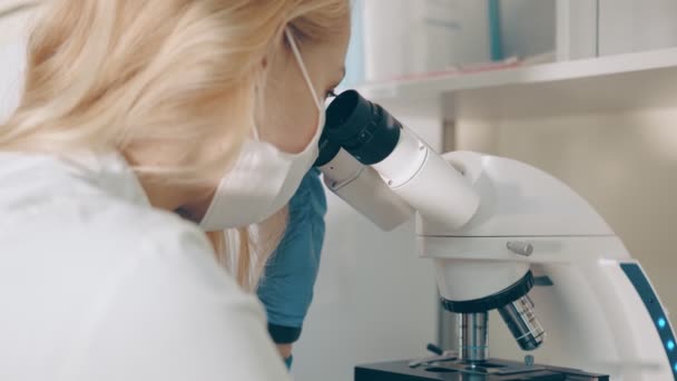 Microbiologo scienziato esamina campioni di sangue biologico al microscopio. Ricercatrice conduce ricerche al microscopio in laboratorio — Video Stock