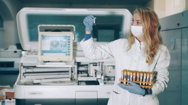 Retrato de una trabajadora de laboratorio con tubos de muestra de sangre en las manos. Laboratorio para el estudio de muestras bioquímicas de sangre. Científico de laboratorio examina muestras del virus. — Vídeo de stock