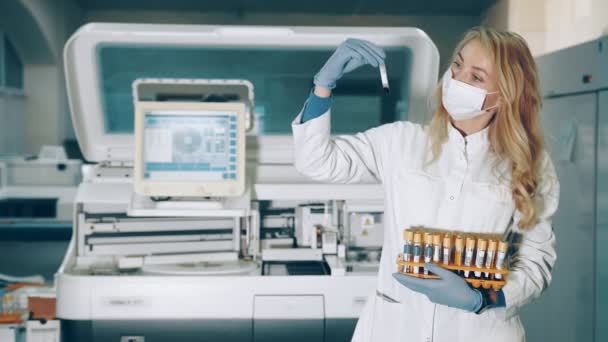 Retrato de una trabajadora de laboratorio con tubos de muestra de sangre en las manos. Laboratorio para el estudio de muestras bioquímicas de sangre. Científico de laboratorio examina muestras del virus. — Vídeo de stock