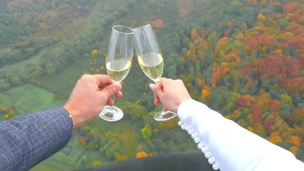 Una giovane coppia tiene tra le mani bicchieri di champagne su uno sfondo di foresta autunnale che vola su un palloncino. Avvicinamento delle mani degli sposi che tengono lo champagne. — Video Stock