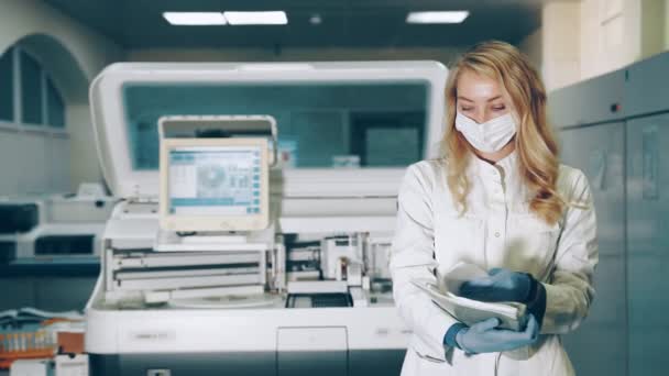 Retrato de un trabajador de laboratorio. Médico femenino en máscara médica protectora en laboratorio hojea registros en carpeta con documentos. — Vídeo de stock