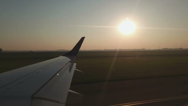 Widok przez okno samolotu przed startem. Skrzydło samolotu o wschodzie słońca na lotnisku. Samolot przygotowuje się do lotu i ma widok na pas startowy z okna samolotu. — Wideo stockowe