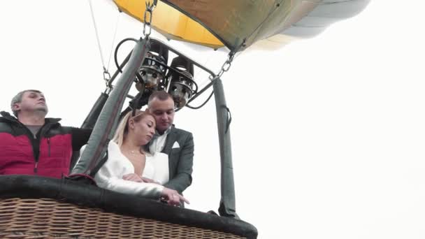 As noivas voam em um balão acima das nuvens. A noiva e o noivo pegam um pau de selfie em um balão em um fundo de nascer do sol sobre as nuvens. Casamento sobre as nuvens. — Vídeo de Stock