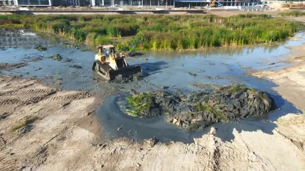 空中の景色大きなブルドーザーは、茂みや沼から湖の底をきれいにします。緑藻から湖の底をきれいにする。重機の作業. — ストック動画