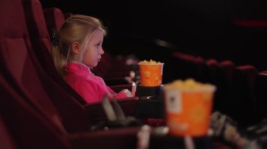 Sinemada yalnız küçük bir kız sinema ekranına bakıyor. Sinemada bir çocuk filmi ya da çizgi film izlemek..