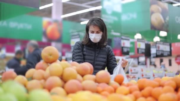 スーパーの保護マスクの若い女性は果物を選択し、ビニール袋に入れます。スーパーマーケットで果物。店舗や市場での買い物. — ストック動画
