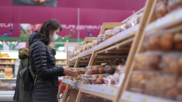 Mujer en el supermercado durante la cuarentena en una máscara protectora compra pan. Compras en un supermercado. Mujer comprando productos de panadería en una panadería de supermercados — Vídeo de stock