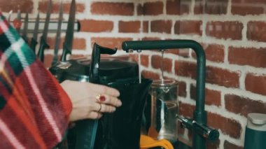 Elektrikli su ısıtıcısında arıtılmış su toplayan kadın. Bir su akıntısı musluktan çaydanlığa akar..