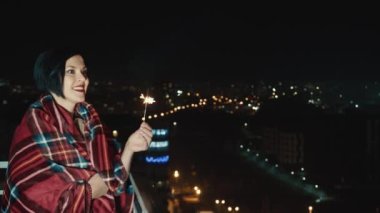 Gece şehrinin arka planında elinde maytapla mutlu bir kadın. Yalnız kutluyoruz. Yalnız bir kadın yalnızlığı mutlu bir şekilde kutlar. Kadınların mutluluğu..