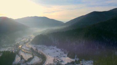 Kış mevsiminde güneşin doğuşu kışın dağların üzerinde olur. Dağlar karla kaplı ve vadide hafif sis var.