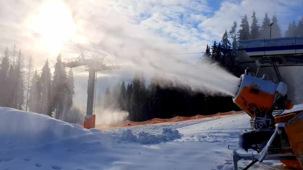 Snökanon på en skidort. Snömaskin producerar konstgjord snö mot bakgrund av solljus och skidliftar. Fantastisk utsikt över skapandet av konstgjord snö. Skidanläggningarnas arbete. — Stockvideo