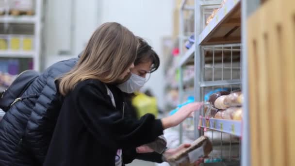 Mom and her baby together supermarket during quarantine in a protective mask buys bread. Shopping in a supermarket. Mom buys bread and the child helps mom buy bread — Stock Video