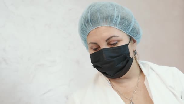 Vrouw met een zwart masker zittend in het dokterskantoor en kijkend naar de camera. Portret van een man met een zwart medisch masker op zijn gezicht. — Stockvideo