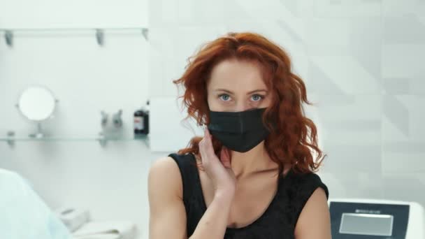 Femme dans un masque noir assis dans le bureau des médecins et regardant la caméra. Portrait d'un homme portant un masque médical noir sur le visage. — Video