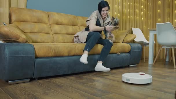 Kobieta odpoczywająca w domu na kanapie i odkurzacz robotów odkurzający pokój. Gdy robot ucieka, kobieta odpoczywa. Przyszłość w sprzątaniu pokoju. — Wideo stockowe