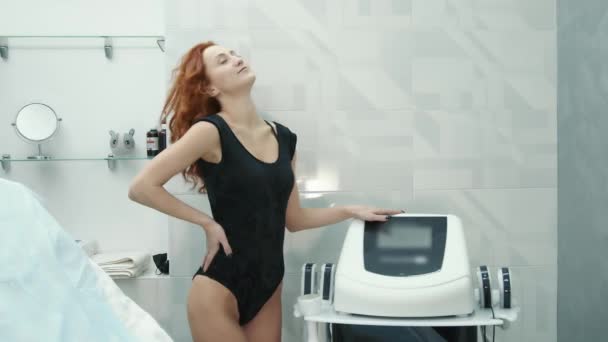 Flicka står på en soffa i en skönhetssalong efter hudföryngring förfaranden. Glad vit kvinna sitter med ryggen mot kameran i en skönhetssalong. — Stockvideo