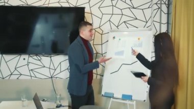 Kuruldaki ofis çalışanları şirketin performansını artırmak için programları tartışıyor. Parlak ofis konferans odasında sunum ekipmanlarının yanında duran meslektaşlar.